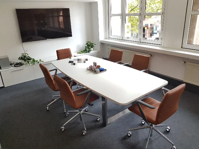 Besprechungsraum mit weißem Tisch, braunen Lederstühlen und Bildschirm an der Wand